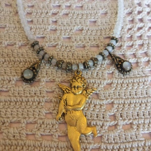 May include: A gold-toned cherub pendant necklace with a white beaded chain and three teardrop-shaped stones.