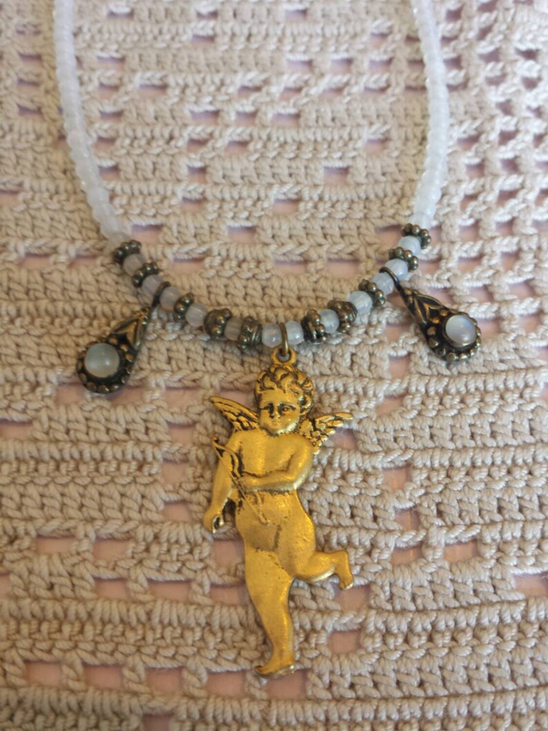 May include: A gold-toned cherub pendant necklace with a white beaded chain and three teardrop-shaped stones.