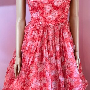 K&ouml;nnte beinhalten: Ein Vintage-Kleid in Rosa und Wei&szlig; mit Blumenmuster, vollem Rock und Spaghettitr&auml;gern. Das Kleid ist aus einem durchsichtigen Stoff gefertigt und hat einen zarten Blumendruck.