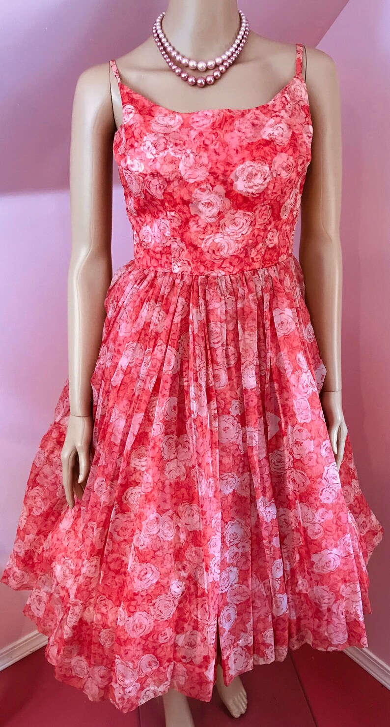 K&ouml;nnte beinhalten: Ein Vintage-Kleid in Rosa und Wei&szlig; mit Blumenmuster, vollem Rock und Spaghettitr&auml;gern. Das Kleid ist aus einem durchsichtigen Stoff gefertigt und hat einen zarten Blumendruck.