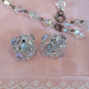 May include: A delicate crystal necklace and matching earrings. The necklace is made of small, faceted crystals strung on a silver chain. The earrings are cluster style, with multiple crystals arranged in a ball shape.