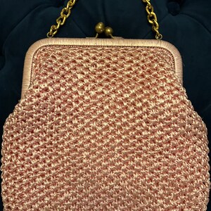 May include: A pink crocheted clutch bag with a gold chain strap and a brass clasp.