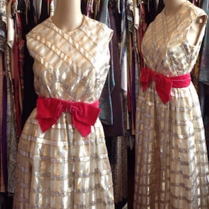 K&ouml;nnte beinhalten: Ein &auml;rmelloses Kleid mit einem gold- und silberfarbenen Muster. Das Kleid hat eine rote Samtschleife an der Taille.
