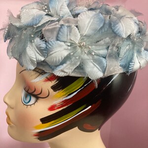 May include: A light blue hat with a flower design. The hat is made of fabric and has a net-like material on top. The hat is sitting on a mannequin's head.