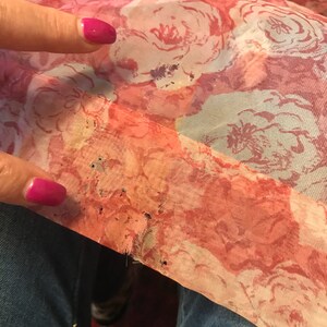 K&ouml;nnte beinhalten: Ein rosa-wei&szlig;er Blumenstoff mit ein paar kleinen L&ouml;chern. Der Stoff ist am Rand leicht ausgefranst.