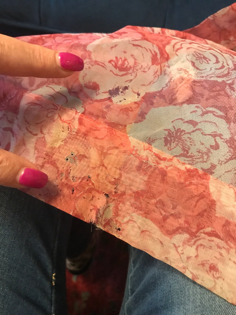 K&ouml;nnte beinhalten: Ein rosa-wei&szlig;er Blumenstoff mit ein paar kleinen L&ouml;chern. Der Stoff ist am Rand leicht ausgefranst.