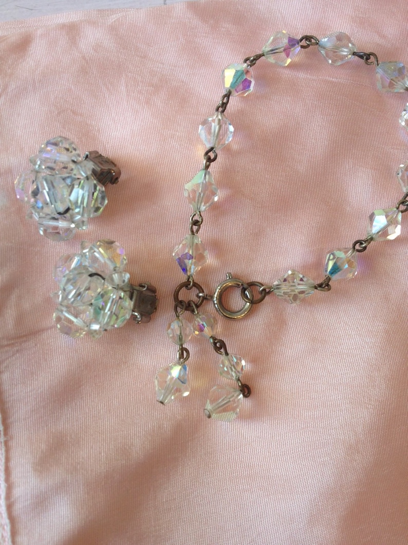 May include: A set of iridescent crystal jewelry featuring a bracelet and a pair of clip-on earrings. The bracelet has a silver clasp and is made of faceted crystal beads. The earrings are also made of faceted crystal beads and have a silver clip.