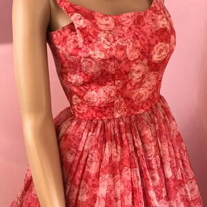 K&ouml;nnte beinhalten: Ein Vintage-Kleid in Rosa und Wei&szlig; mit Blumenmuster, vollem Rock und d&uuml;nnen Tr&auml;gern. Das Kleid ist aus einem durchsichtigen Stoff gefertigt und hat einen zarten, femininen Look.