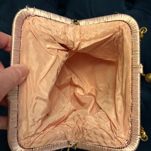 May include: A pink satin evening bag with a gold clasp and chain. The bag is open and the inside is lined with a pale pink fabric.