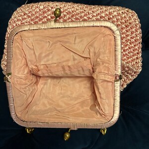 May include: A pink crocheted purse with a gold clasp and a satin lining.