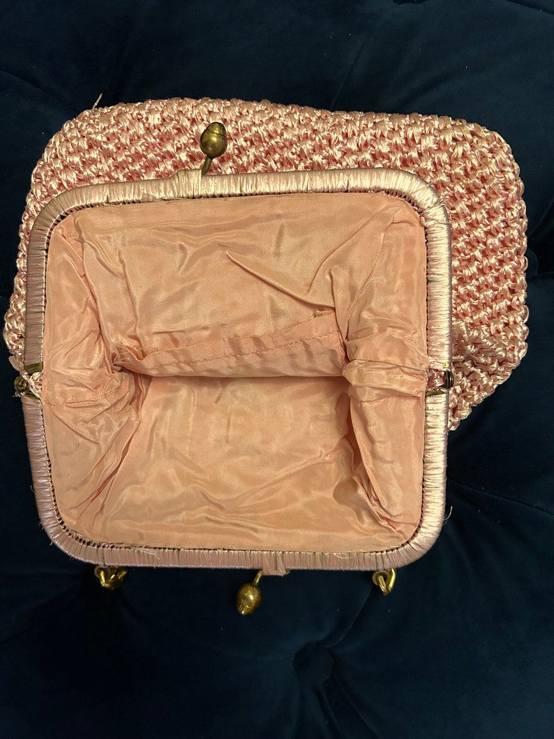 May include: A pink crocheted purse with a gold clasp and a satin lining.