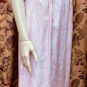 May include: A pink sleeveless dress with a floral pattern. The dress has a fitted bodice and a flowing skirt with a slit in the front.