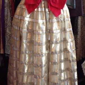 K&ouml;nnte beinhalten: Ein gold-wei&szlig;es Paillettenkleid mit einer roten Samtschleife an der Taille.