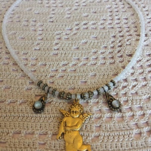 May include: A white beaded necklace with a gold cherub pendant and two smaller gold teardrop pendants with iridescent stones.