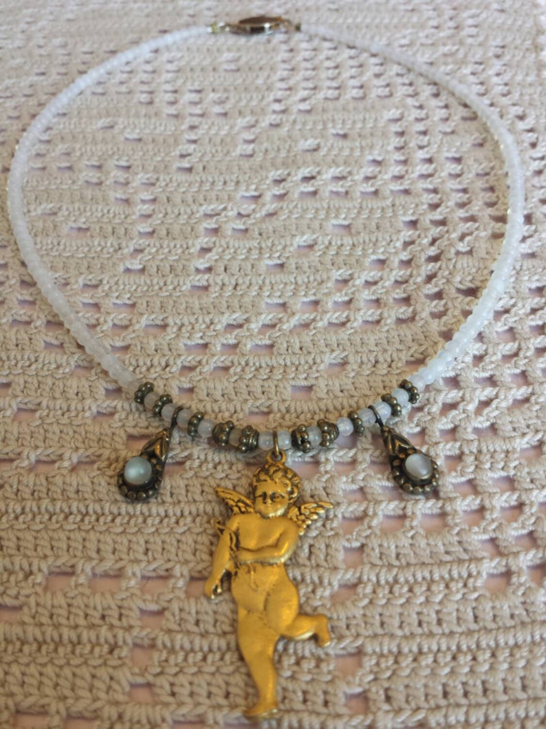 May include: A white beaded necklace with a gold cherub pendant and two smaller gold teardrop pendants with iridescent stones.