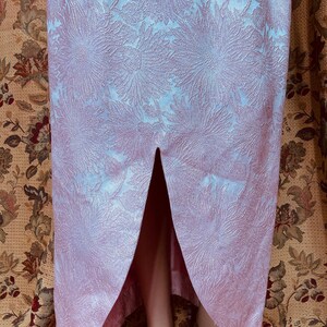 May include: A pink maxi dress with a floral pattern and a front slit. The dress is made of a textured fabric.