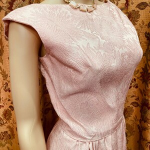 May include: A pink sleeveless dress with a floral pattern. The dress has a scoop neckline and a fitted bodice. The dress is made of a textured fabric.