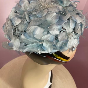 May include: A light blue hat made of fabric flowers and netting. The hat is decorated with small, white beads.