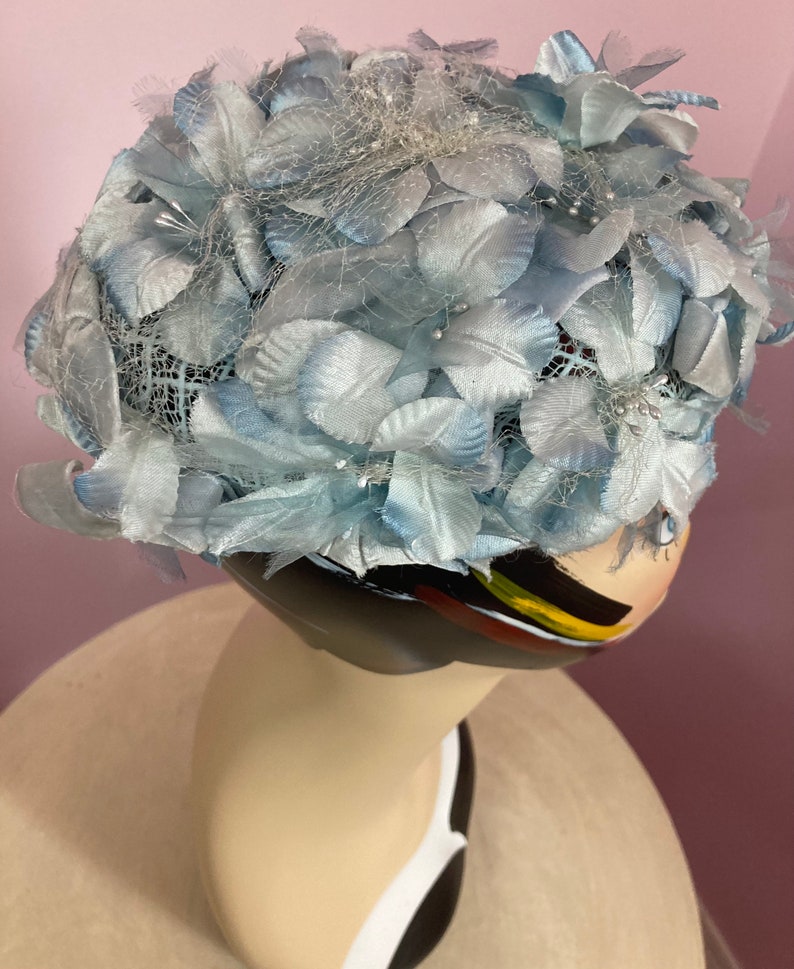 May include: A light blue hat made of fabric flowers and netting. The hat is decorated with small, white beads.