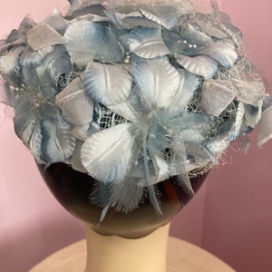 May include: A light blue hat made of fabric flowers and netting. The hat is on a mannequin head.