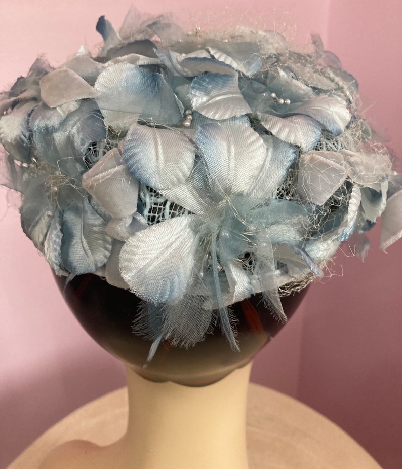 May include: A light blue hat made of fabric flowers and netting. The hat is on a mannequin head.