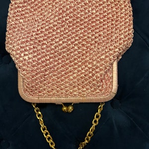 May include: A pink crocheted purse with a gold chain strap and gold clasp.