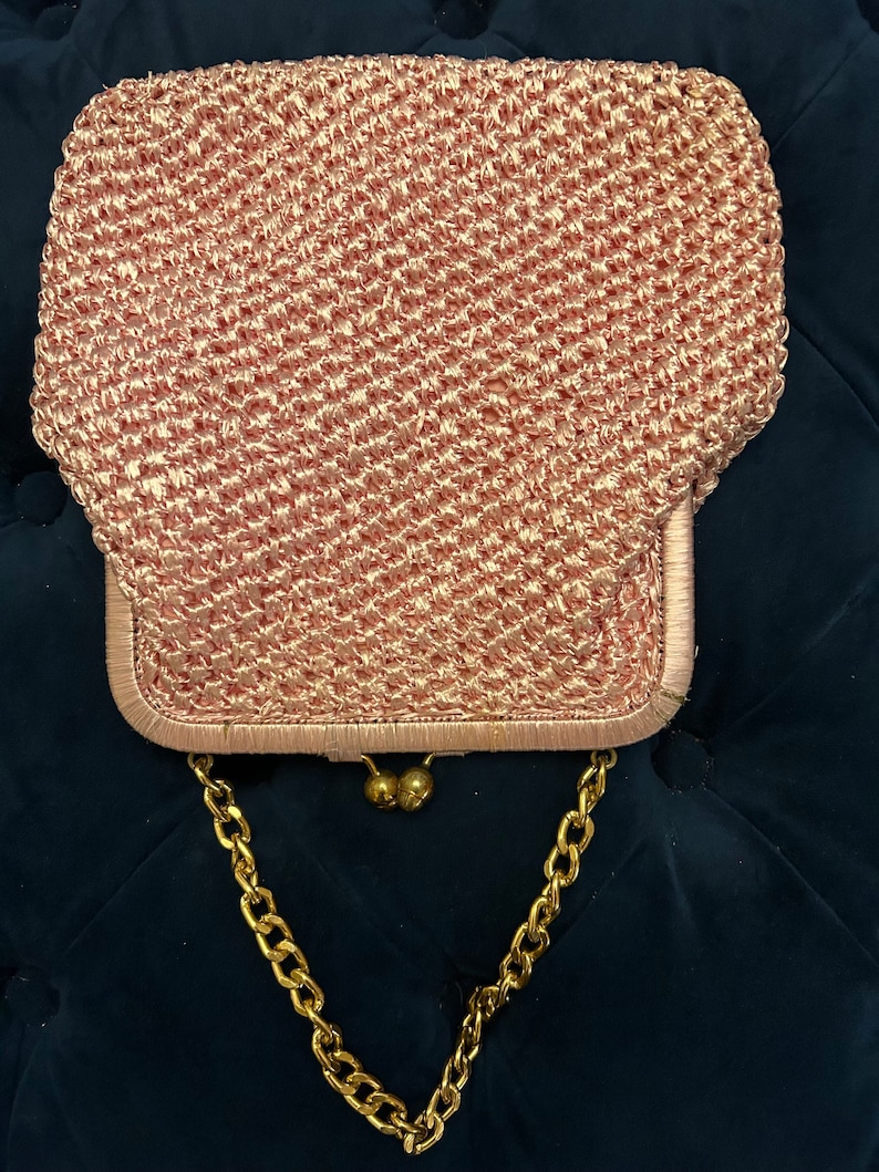 May include: A pink crocheted purse with a gold chain strap and gold clasp.