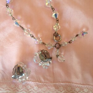 May include: A crystal bracelet with a silver clasp and matching crystal earrings. The jewelry is on a pink fabric background.