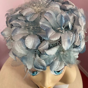 May include: A light blue hat with a floral design. The hat is made of fabric and has a net-like texture. The flowers are made of satin and have a delicate, feminine look.