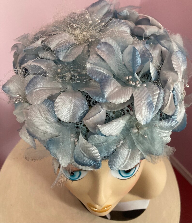 May include: A light blue hat with a floral design. The hat is made of fabric and has a net-like texture. The flowers are made of satin and have a delicate, feminine look.