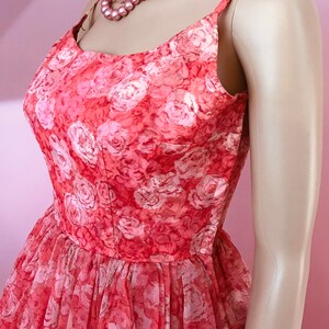 K&ouml;nnte beinhalten: Ein vintage-Kleid in rosa und wei&szlig; mit Blumenmuster, runder Ausschnitt und d&uuml;nnen Tr&auml;gern. Das Kleid ist aus einem durchsichtigen Stoff und hat einen vollen Rock.