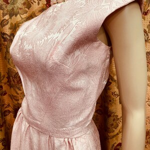 May include: A pink sleeveless dress with a floral pattern. The dress has a scoop neckline and a fitted bodice. The dress is made of a textured fabric.