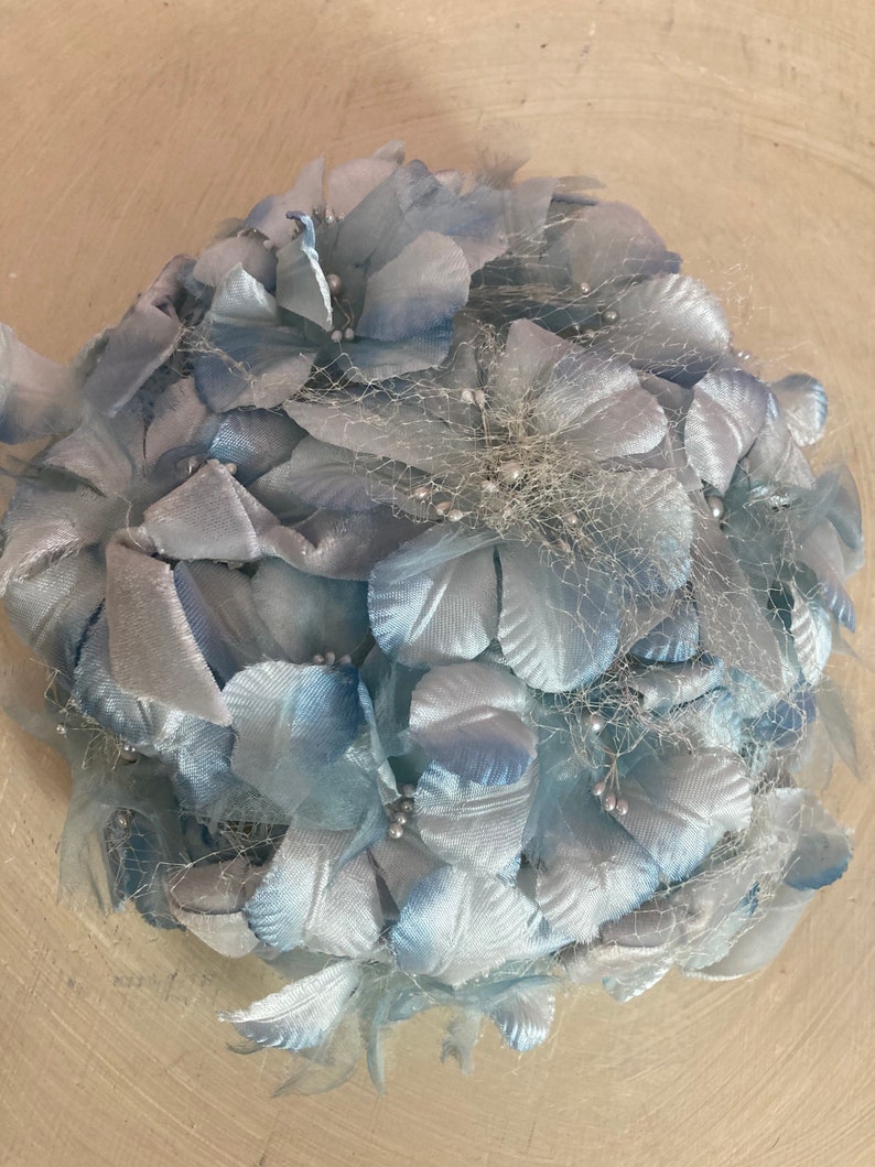 May include: A light blue vintage hat made of fabric flowers and netting. The hat is decorated with small silver beads.