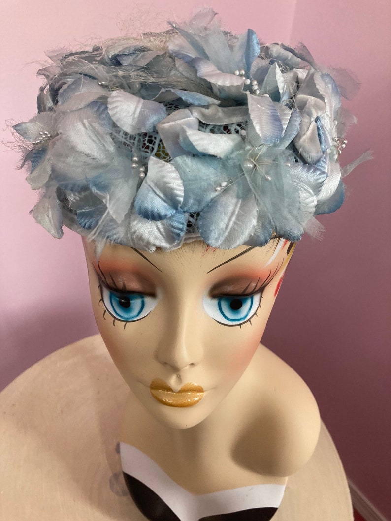 May include: A light blue hat with a flower design. The hat is made of fabric and has a net-like texture. The hat is decorated with small white beads.