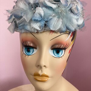 May include: A light blue hat with a flower design. The hat is made of fabric and has a net-like texture. The hat is decorated with small white beads.