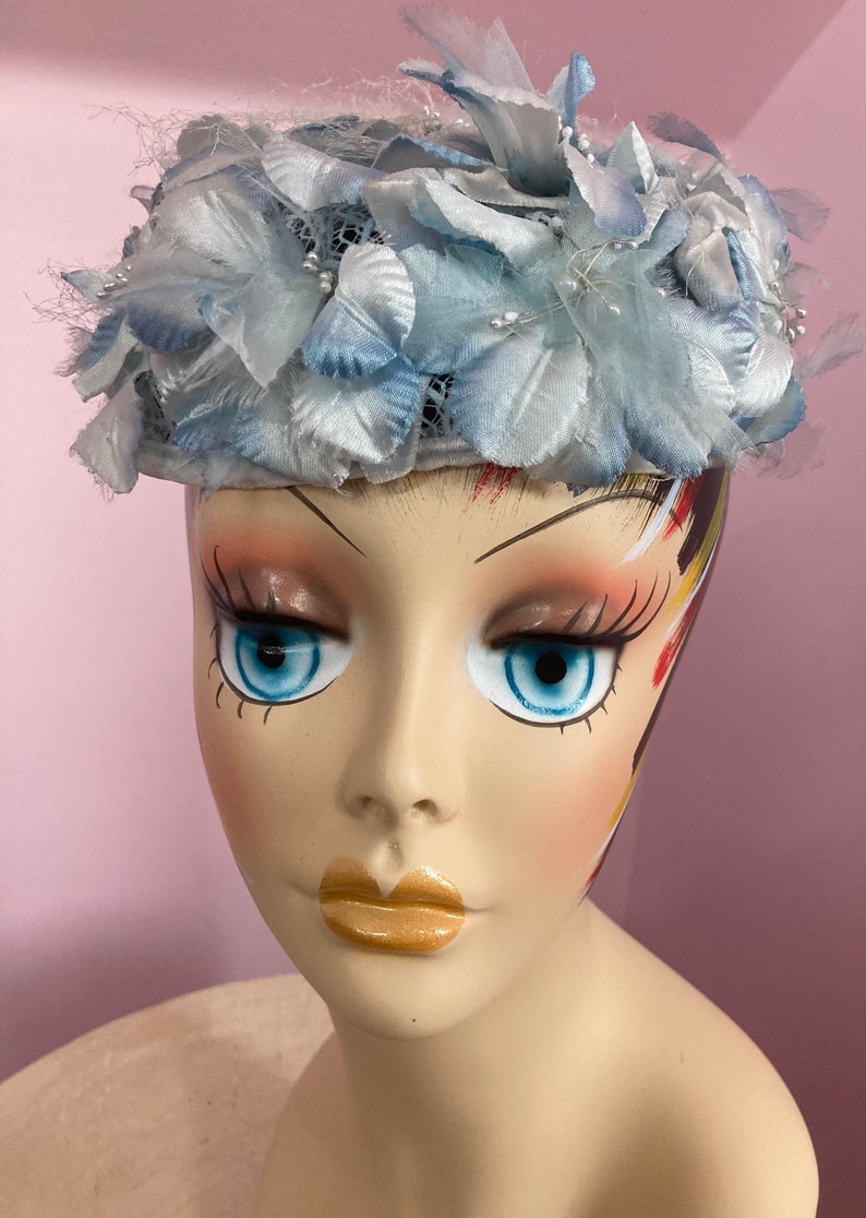 May include: A light blue hat with a flower design. The hat is made of fabric and has a net-like texture. The hat is decorated with small white beads.