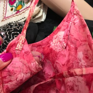 K&ouml;nnte beinhalten: Nahaufnahme eines rosa Stoffes mit floralem Muster und einem d&uuml;nnen rosa Band, das entlang der Kante gen&auml;ht ist. Der Stoff ist gerafft und gefaltet, wodurch das Detail des Musters sichtbar wird.