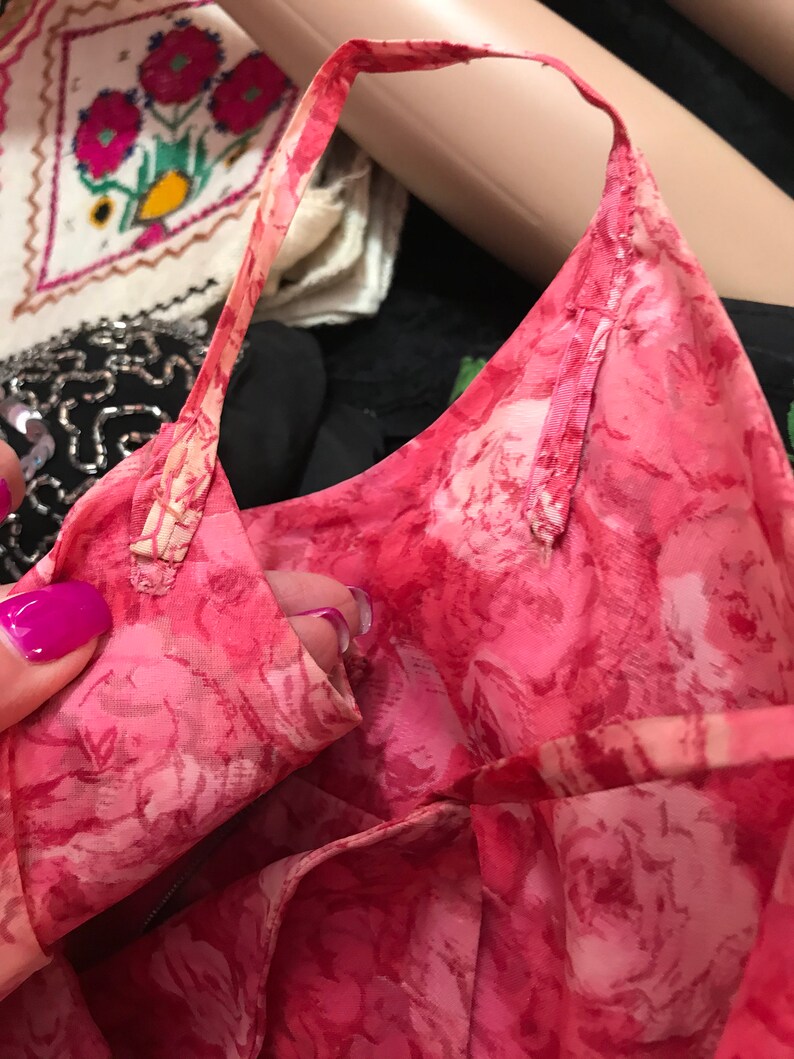 K&ouml;nnte beinhalten: Nahaufnahme eines rosa Stoffes mit floralem Muster und einem d&uuml;nnen rosa Band, das entlang der Kante gen&auml;ht ist. Der Stoff ist gerafft und gefaltet, wodurch das Detail des Musters sichtbar wird.