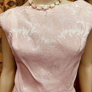 May include: A pink sleeveless dress with a floral pattern. The dress has a scoop neckline and a fitted bodice. The dress is made of a textured fabric.