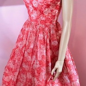 K&ouml;nnte beinhalten: Ein korallenfarbenes Kleid mit wei&szlig;em Blumenmuster. Das Kleid hat einen runden Ausschnitt und ist &auml;rmellos. Es ist aus einem leichten Stoff gefertigt und hat einen vollen Rock.