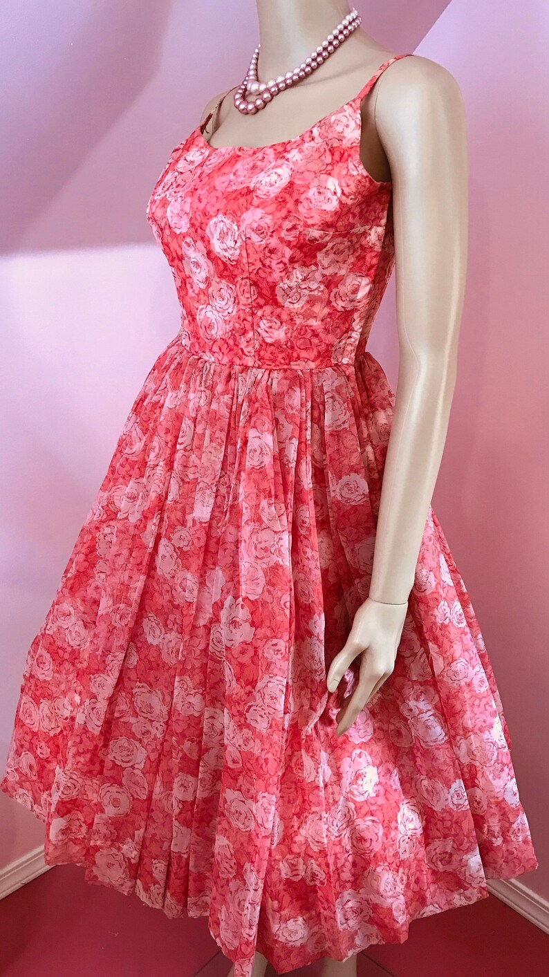 K&ouml;nnte beinhalten: Ein korallenfarbenes Kleid mit wei&szlig;em Blumenmuster. Das Kleid hat einen runden Ausschnitt und ist &auml;rmellos. Es ist aus einem leichten Stoff gefertigt und hat einen vollen Rock.