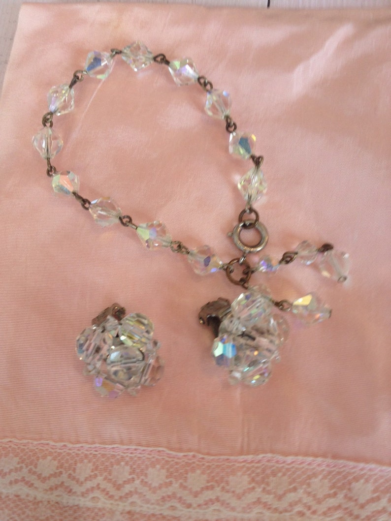 May include: A set of vintage crystal jewelry featuring a bracelet and a pair of earrings. The bracelet is made of clear crystal beads strung on a silver chain. The earrings are also made of clear crystal beads and have a silver clasp.
