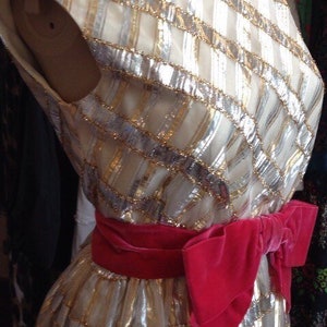 K&ouml;nnte beinhalten: Ein wei&szlig;es Kleid mit goldenen und silbernen Pailletten, einem rosa Samtband und einem taillierten Oberteil.