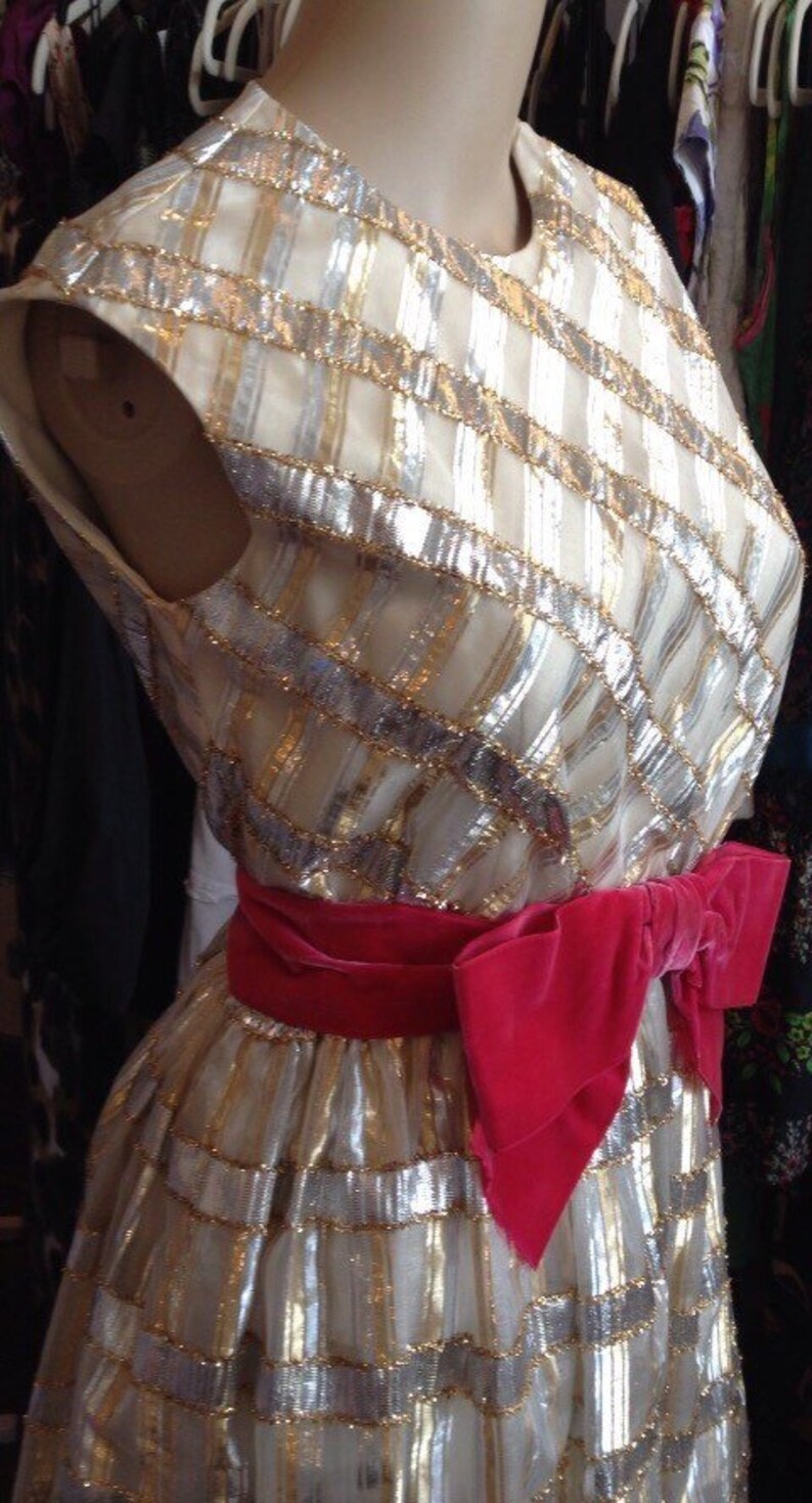K&ouml;nnte beinhalten: Ein wei&szlig;es Kleid mit goldenen und silbernen Pailletten, einem rosa Samtband und einem taillierten Oberteil.