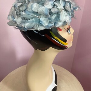 May include: A light blue hat with a net and feather trim. The hat is on a mannequin head.