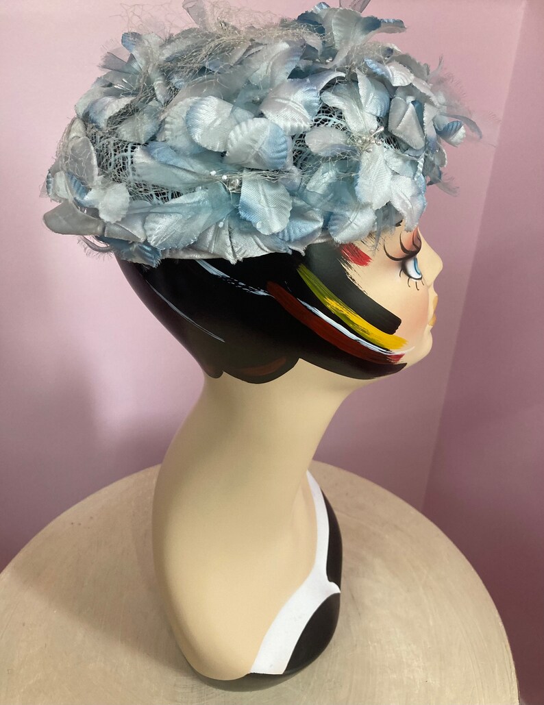 May include: A light blue hat with a net and feather trim. The hat is on a mannequin head.