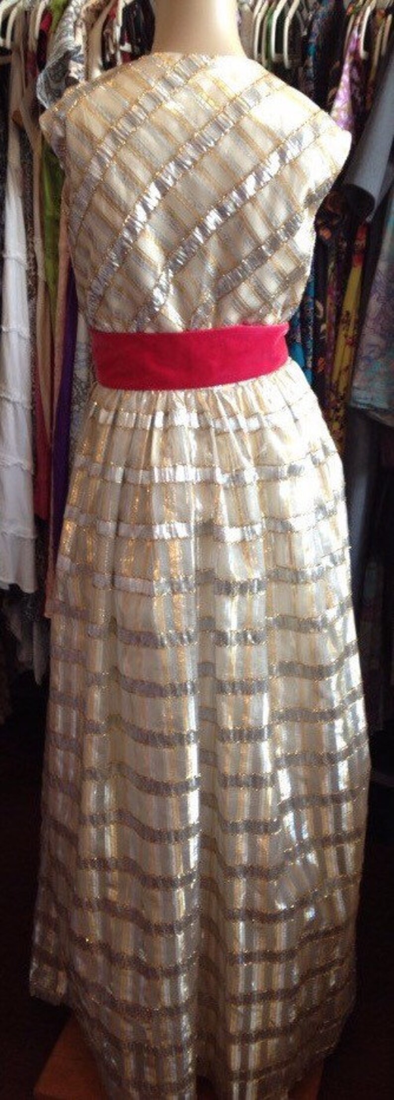 K&ouml;nnte beinhalten: Ein wei&szlig;es Kleid mit goldenen und silbernen Streifen und einer roten Samt-Sch&auml;rpe. Das Kleid ist aus einem gl&auml;nzenden Stoff gefertigt und hat ein tailliertes Oberteil und einen weiten Rock.