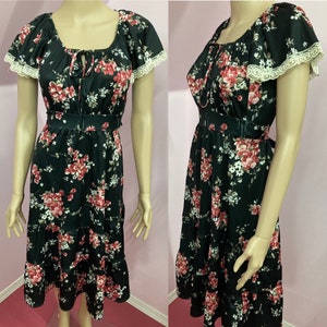 May include: A black floral dress with a ruffled skirt and lace trim on the sleeves. The dress has a tie at the neckline and a belt at the waist.
