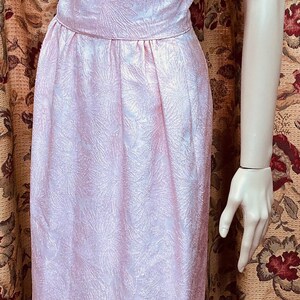 May include: A pink sleeveless dress with a floral pattern. The dress has a fitted bodice and a skirt that falls to the knees. The dress is made of a textured fabric.