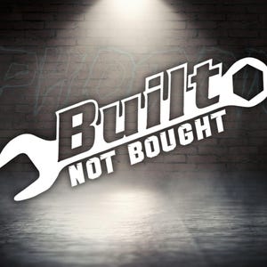 May include: White wrench with the text "Built Not Bought" in black lettering. The wrench is on a dark brick background.